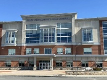 A three-story brick and concrete school building with large windows and an entrance canopy, featuring reliable automatic door maintenance, photographed on a clear day.